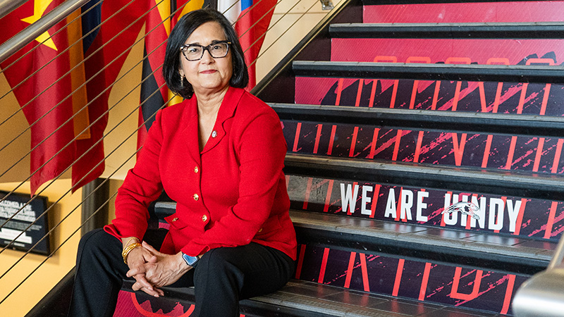 President Singh sitting on the stairs that reads We Are UIndy.