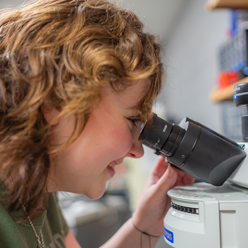 smiling student using a microscope