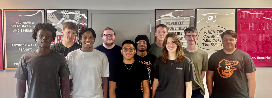diverse group of students smiling in front of a wall with motivational posters.