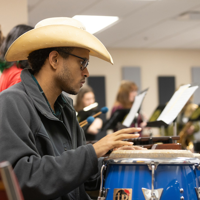 student with cowboy hat playing the bongos