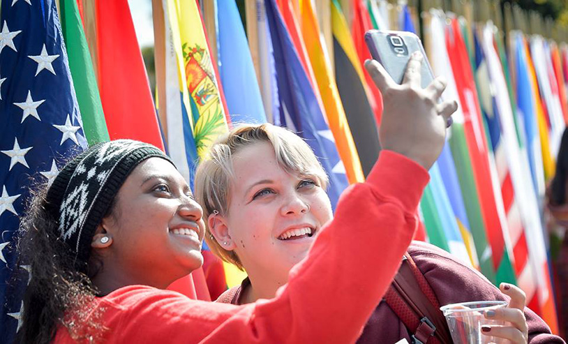 two students taking a photo in front of the flags