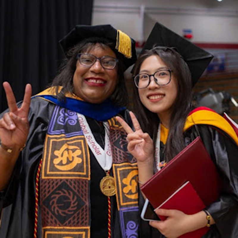 student and professor smiling during graduation ceremonyy