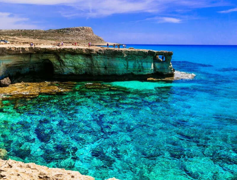 Rocky coastal cliff overlooking clear turquoise water with visible underwater rocks