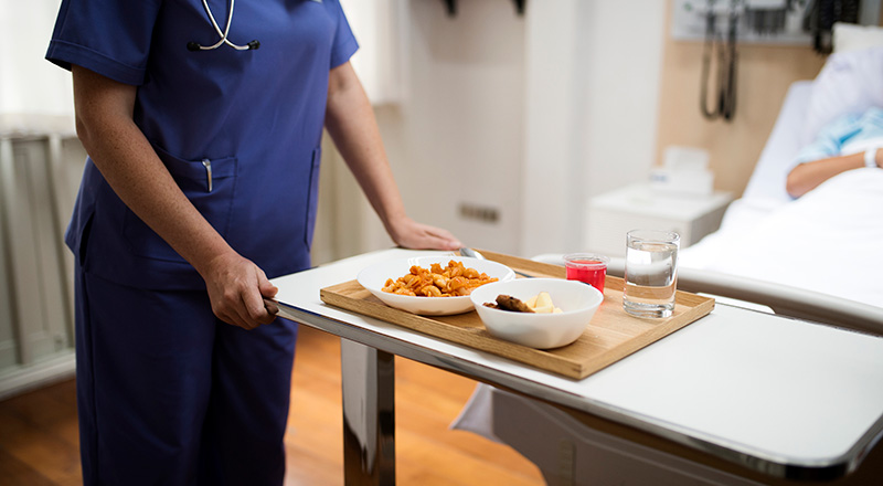 a medical professional brings a tray of food to a patient in a hospital bed