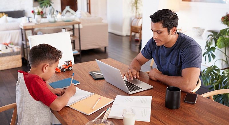 father at home on his laptop with his young son