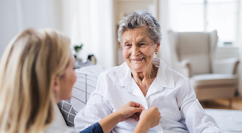 a woman helping an elderly lady button her shirt
