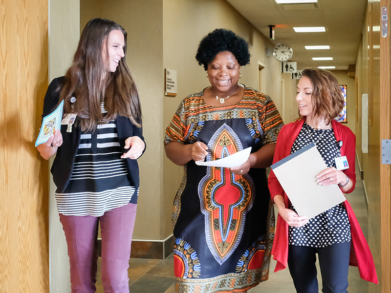 three health professionals walk together down a hallway with paperwork in their hands