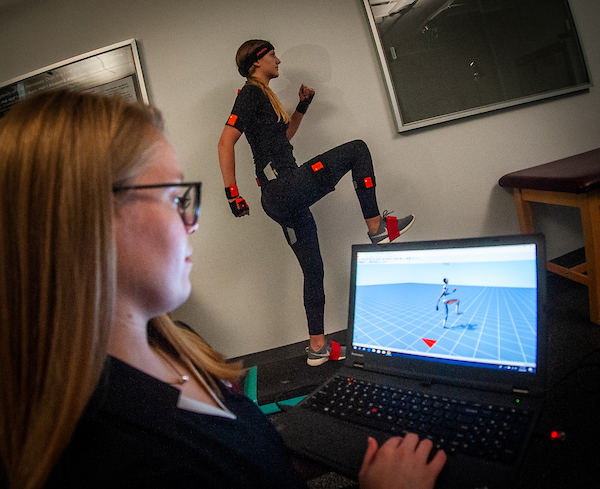 Student with sensors in background, female student looks at computer 