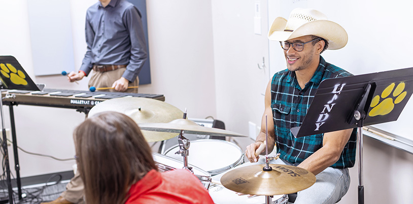 student in a cowboy hat playing the drums
