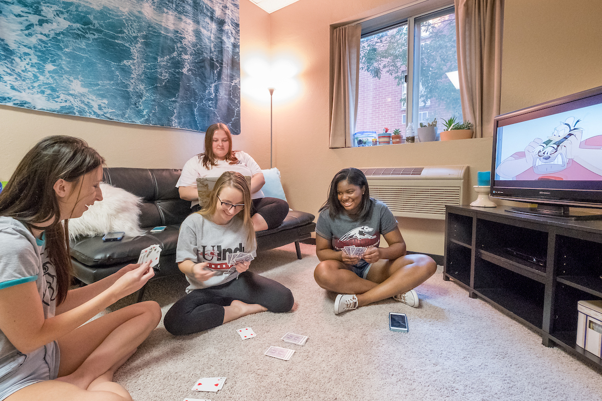 a few female students sitting on the floor playing a card game